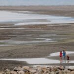 Three people stand in front of the expansive Salt Lake flats, with dried out puddles throughout the landscape